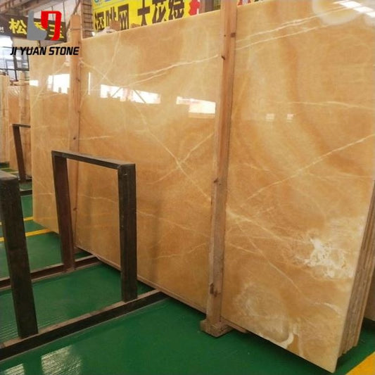 Large polished honey onyx slab with amber tones and cream veining in a stone yard
